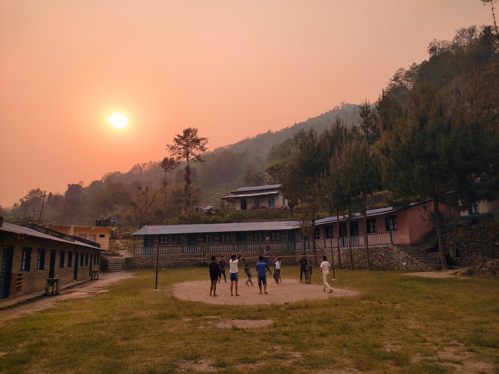 Die Schule in Sotang bei Sonnenuntergang, auf dem Schulhof spielen Menschen Volleyballl