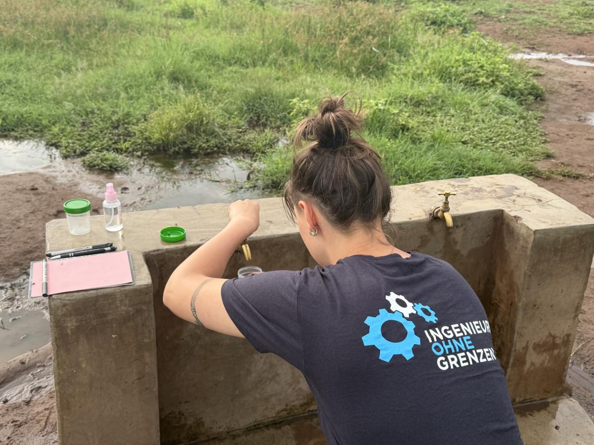 Ein Mitglied von Ingenieure ohne Grenzen entnimmt Wasserproben an einer Wasserentnahmestelle in Olasiti. Die Untersuchung dient der Analyse der Wasserqualität und der bestehenden Wasserversorgung im Rahmen der Projektarbeit.