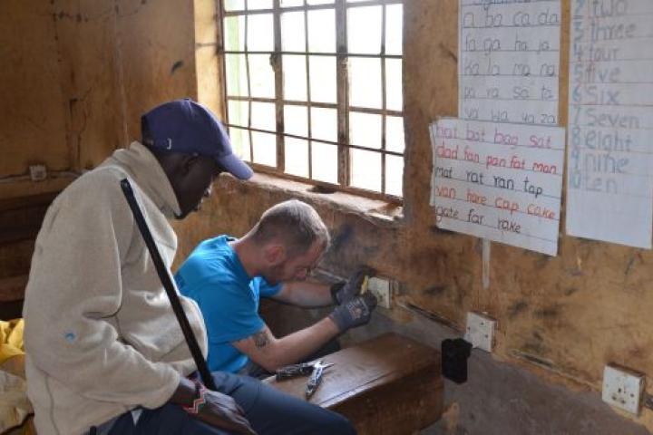 Ein Mitglied von Ingenieure ohne Grenzen arbeitet gemeinsam mit einem lokalen Partner an der Elektroinstallation eines Klassenraums der Olasiti Community School. Die Untersuchung diente der technischen Bestandsaufnahme und Verbesserung der Sicherheit der bestehenden Infrastruktur.