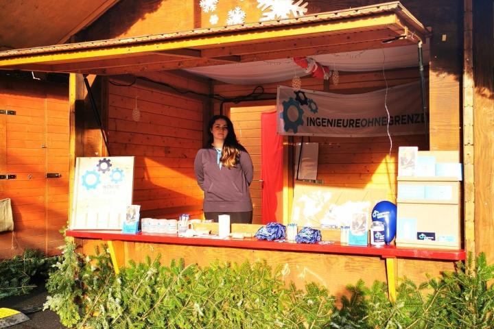 eine hölzerne Hütte eines Weihnachtsmarkt-Standes mit IOG Banner und einer Person hinter der Theke